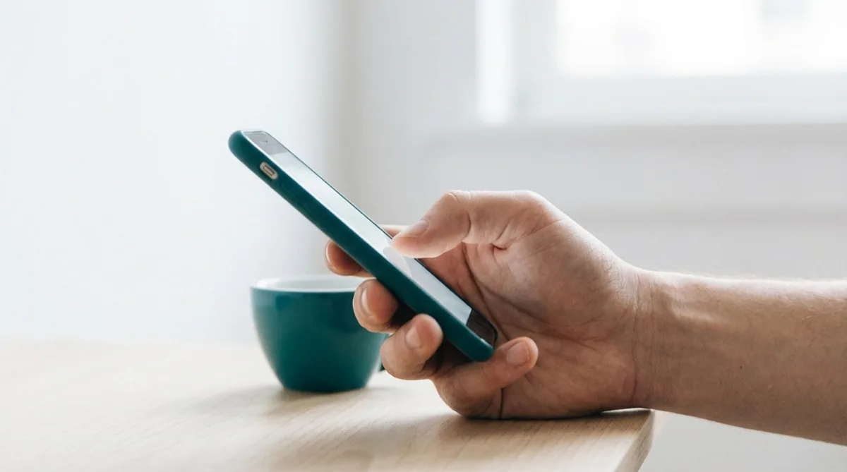 Eine Hand hält ein Smartphone, Daumen auf dem Bildschirm – Smartphone-Daumen Ergotherapie